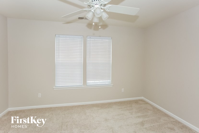 A room with a carpet floor, a ceiling fan, and a window with blinds.