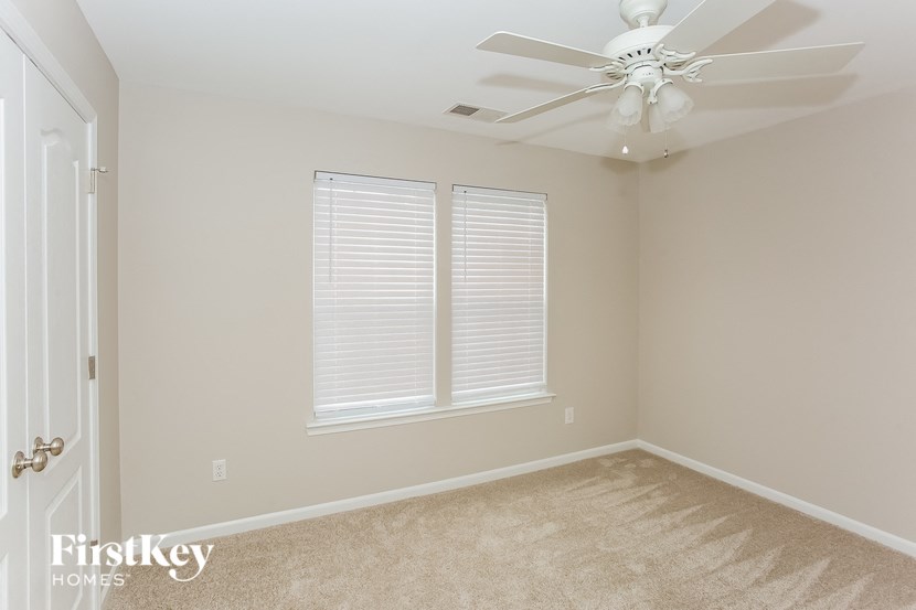 A room with a fan, carpet, and a window with blinds.