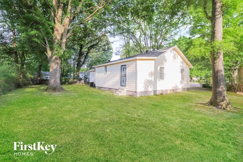 a small white house in the middle of a yard with trees