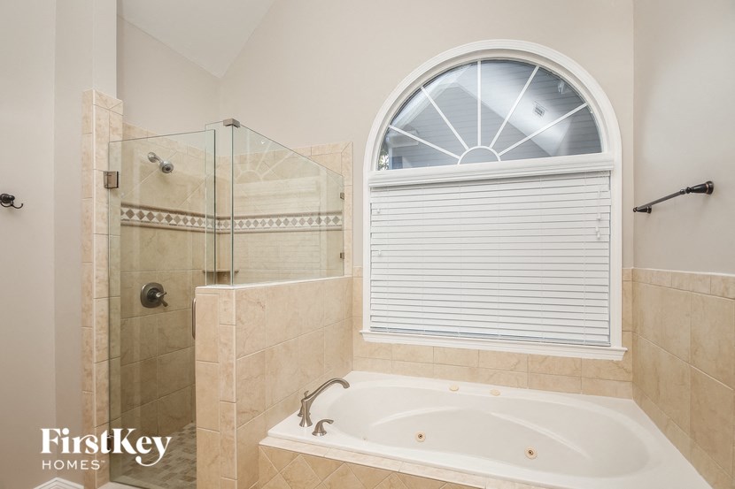 A bathroom with a tub, shower, and a window with blinds.