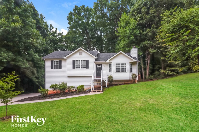 A white house with a black roof is surrounded by greenery.