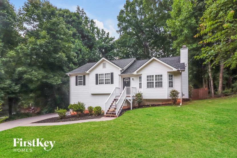 A house with a white exterior and a black roof is surrounded by greenery.