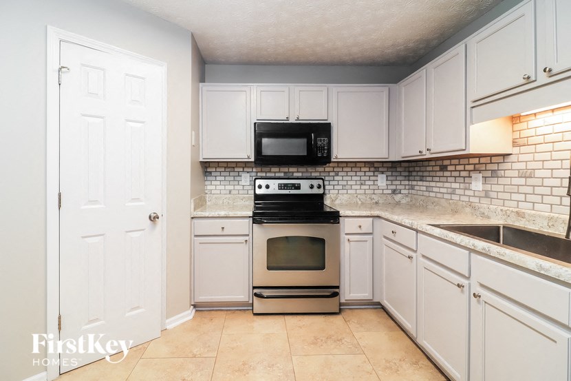 A kitchen with white cabinets and a black microwave above the stove.