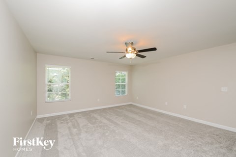 a spacious living room with white carpet and a ceiling fan