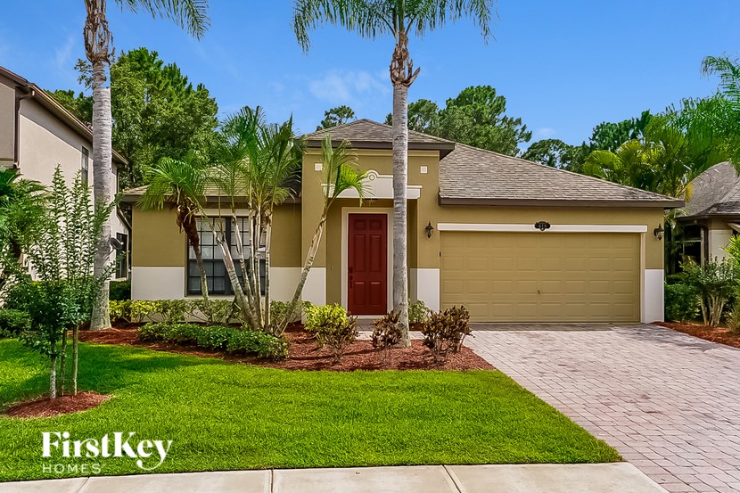 A house with a red door is surrounded by greenery and has a "FirstKey Homes" sign.