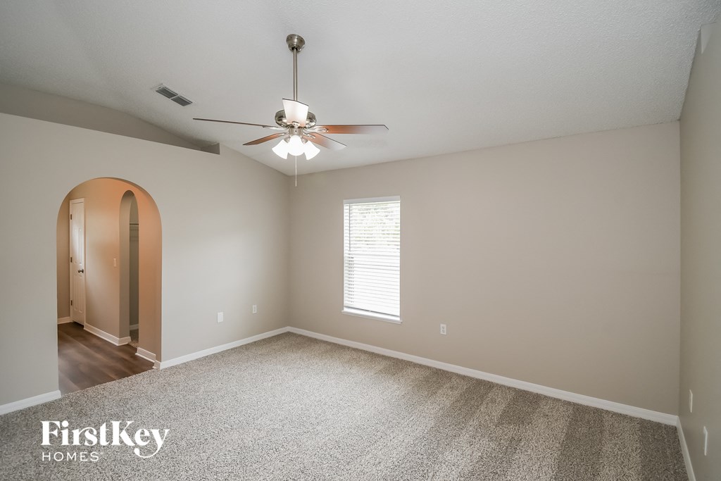 an empty living room with a ceiling fan and a door to a hallway