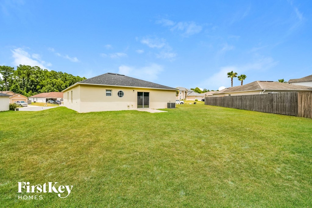 a backyard with a yellow house and a grass field