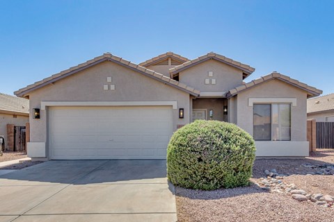 A house with a white garage door and a green bush in front.