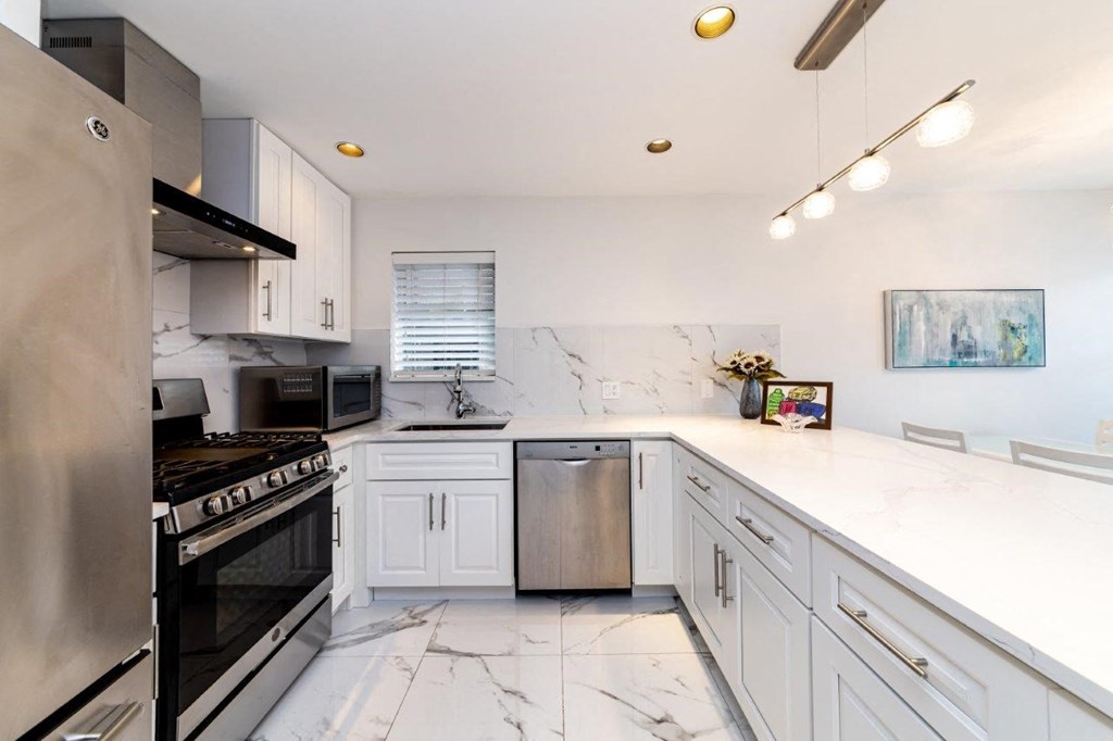 a white kitchen with stainless steel appliances and marble counter tops