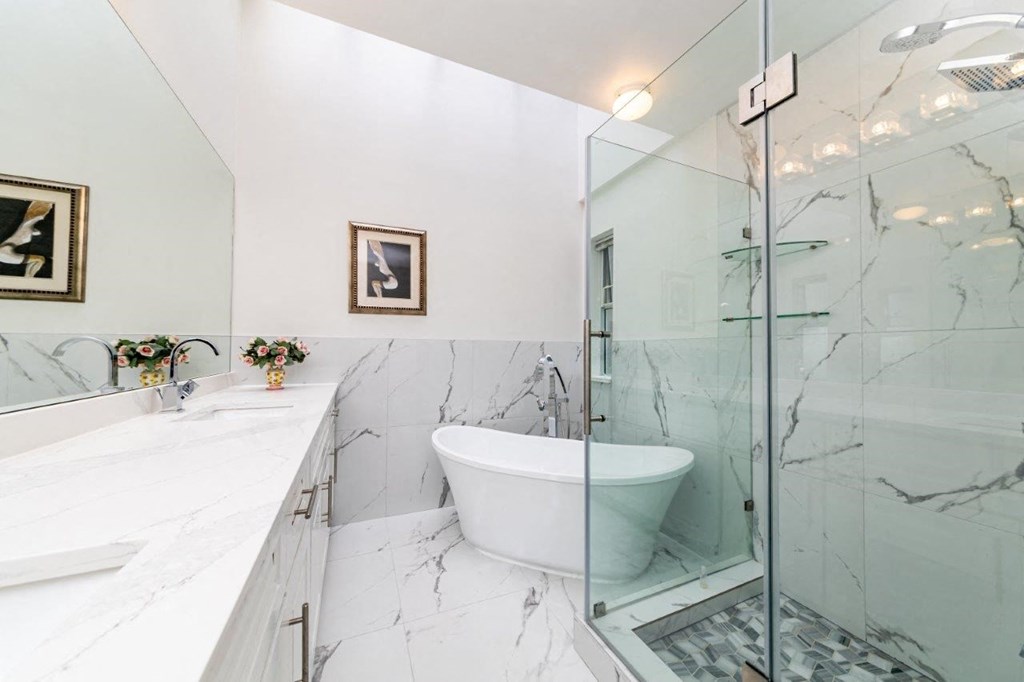 the bathroom has marble floors and walls and a glass shower and tub
