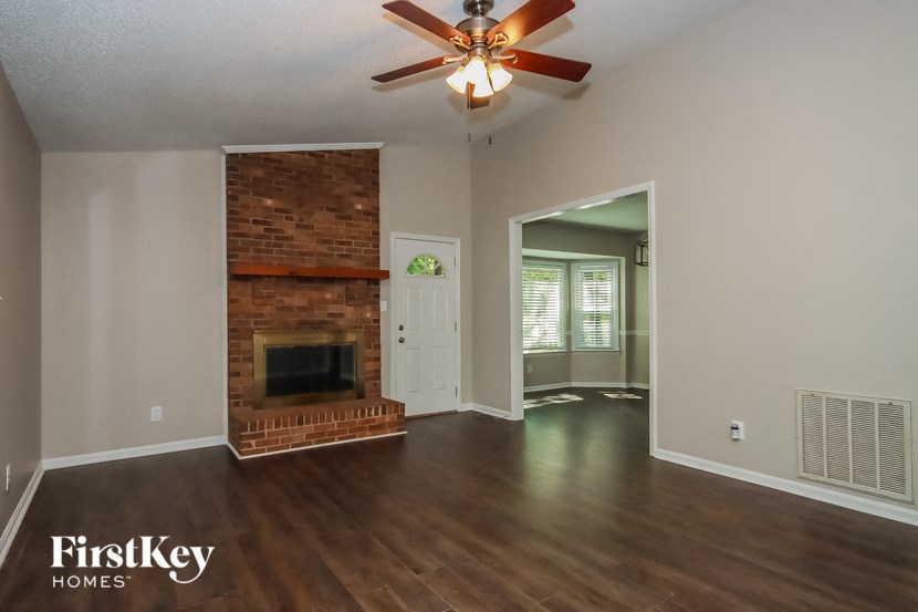an empty living room with a brick fireplace and a ceiling fan