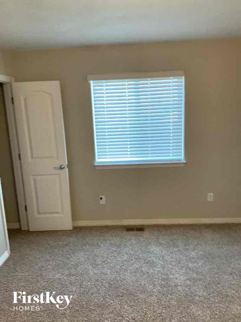 A room with a carpeted floor, a door, and a window with blinds.