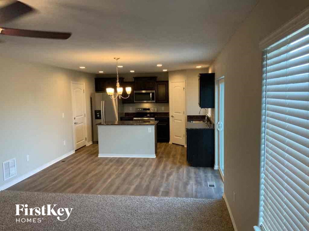 A well-lit kitchen and living room with a carpeted floor and a ceiling fan.