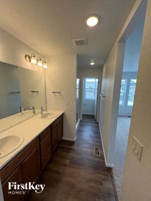 A long, narrow hallway with a row of sinks on the left and a door at the end.