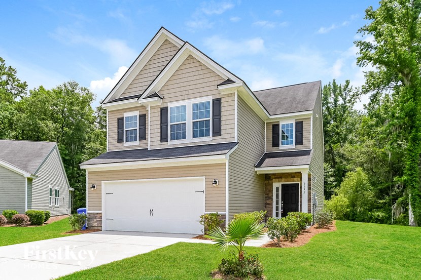 A two-story house with a garage is surrounded by greenery.