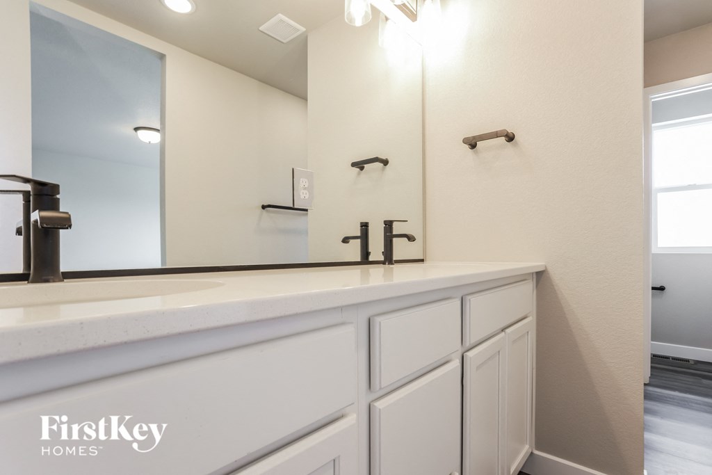 the master bathroom has a large vanity with white cabinets and a large mirror