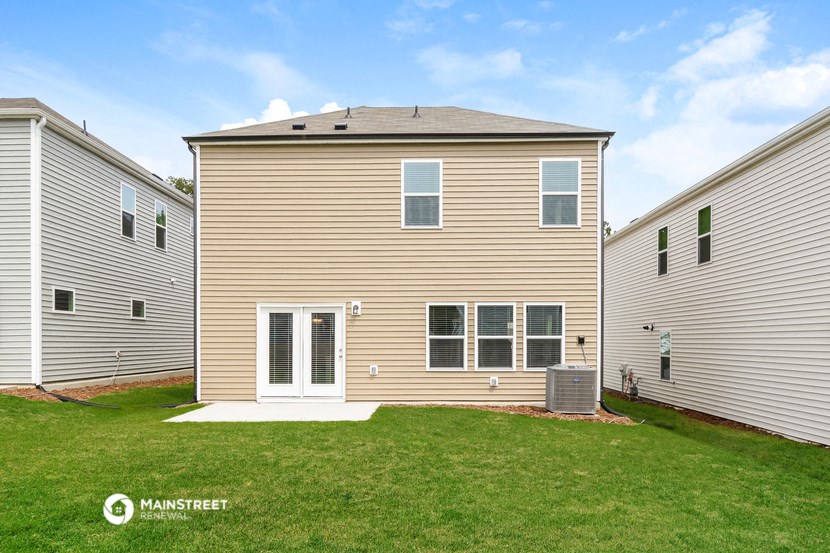 side view of a tan house with white siding and green grass