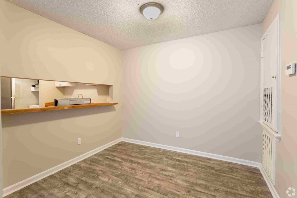 an empty living room with a kitchen in the corner