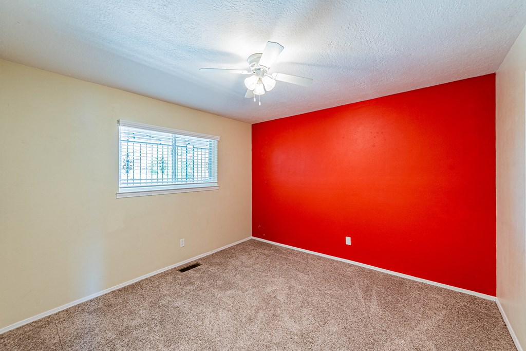 an empty room with a red wall and a ceiling fan