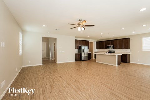 A spacious living room with a kitchen in the background and a ceiling fan above.