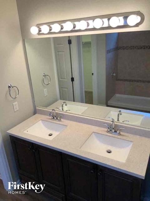 A bathroom with a double sink vanity and a mirror with lights above it.