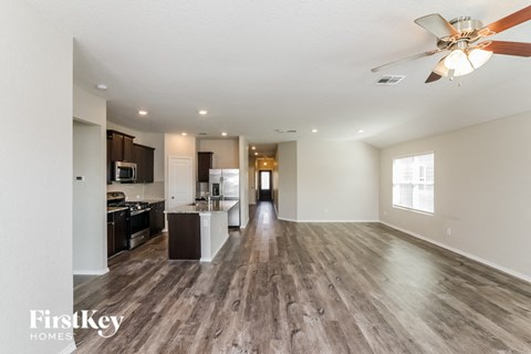 A spacious living room with a kitchen in the background and a wood floor.