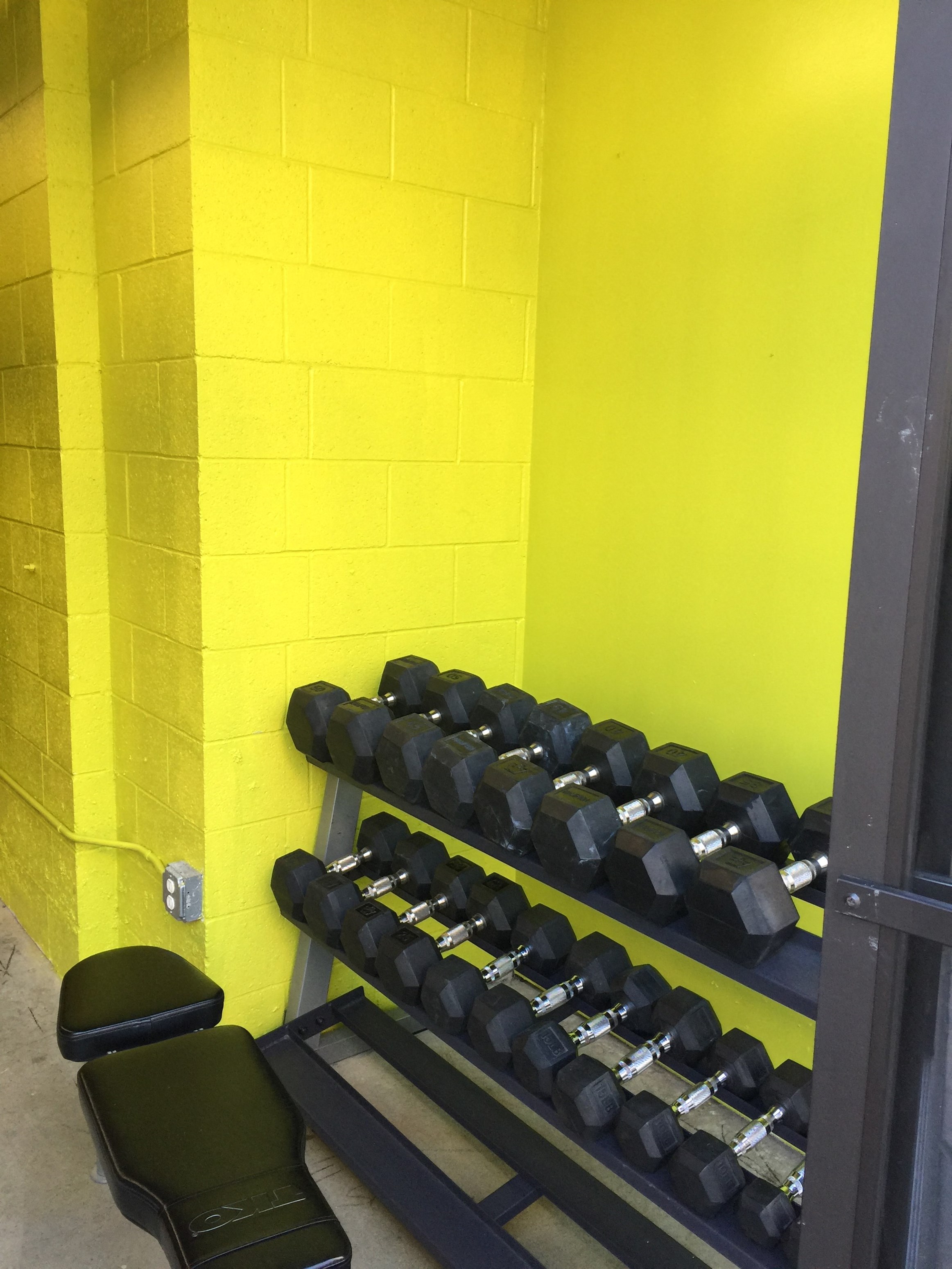 a rack of dumbbells in a gym with a yellow wall