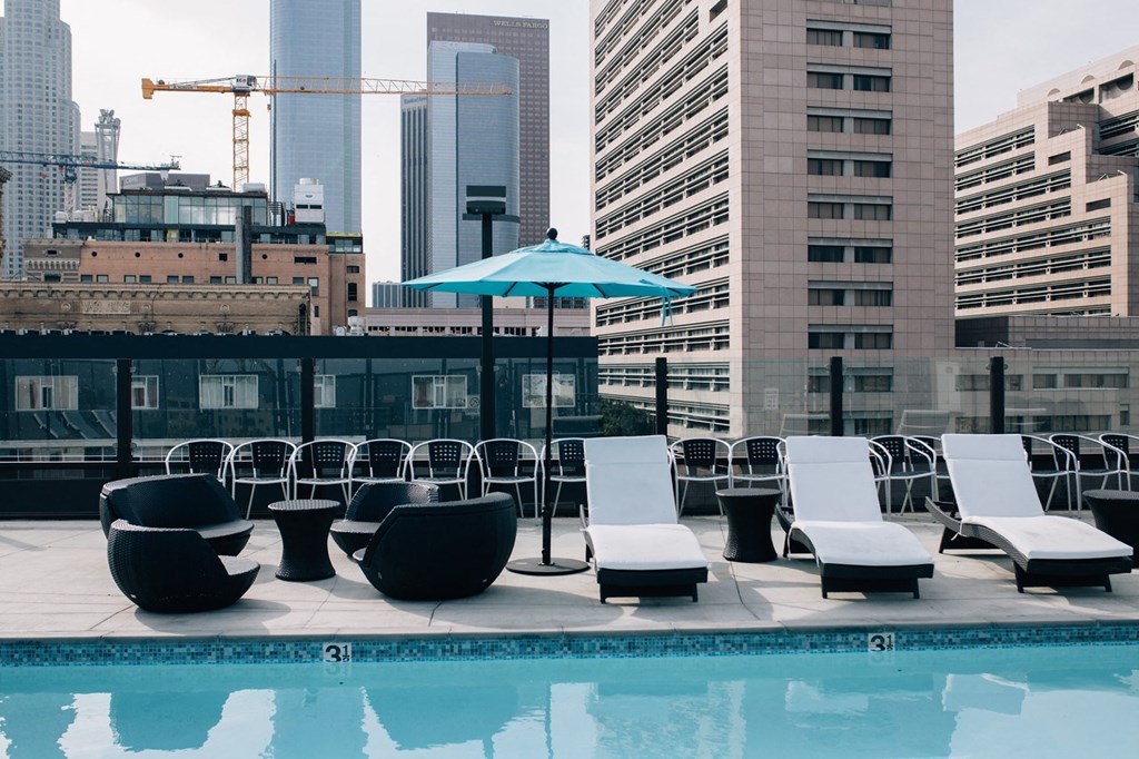 a pool with lounge chairs and an umbrella on a rooftop