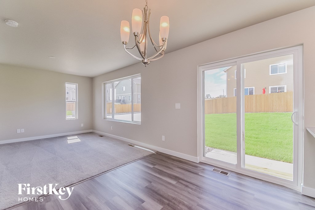 A spacious room with a chandelier and a view of a fence and greenery outside the window.