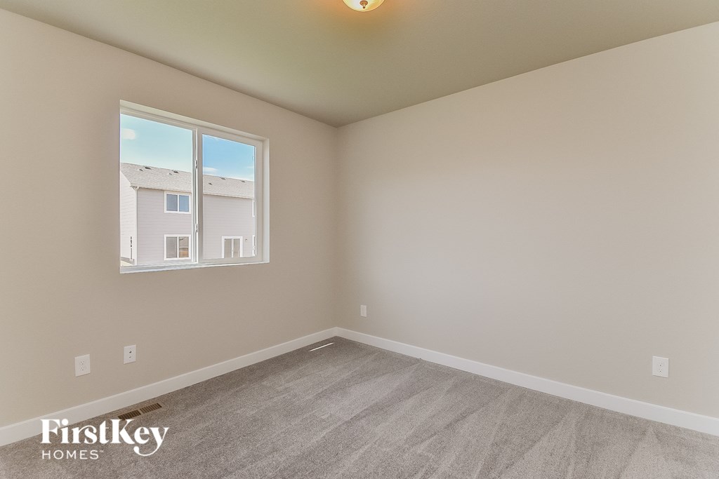 A room with a window showing a building outside and a carpet on the floor.
