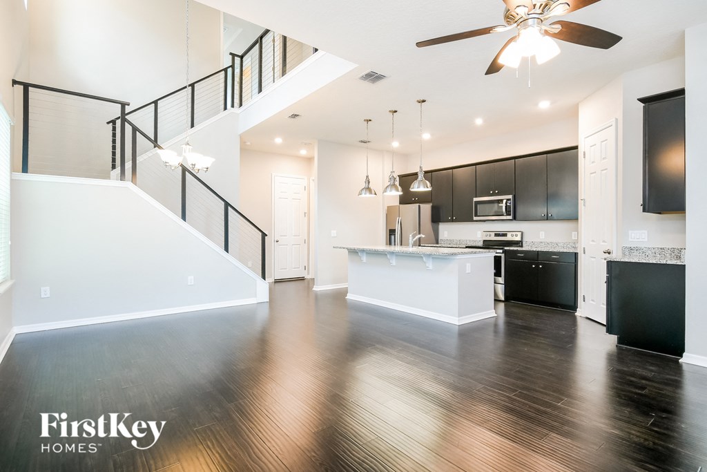 an empty living room with a kitchen and a ceiling fan