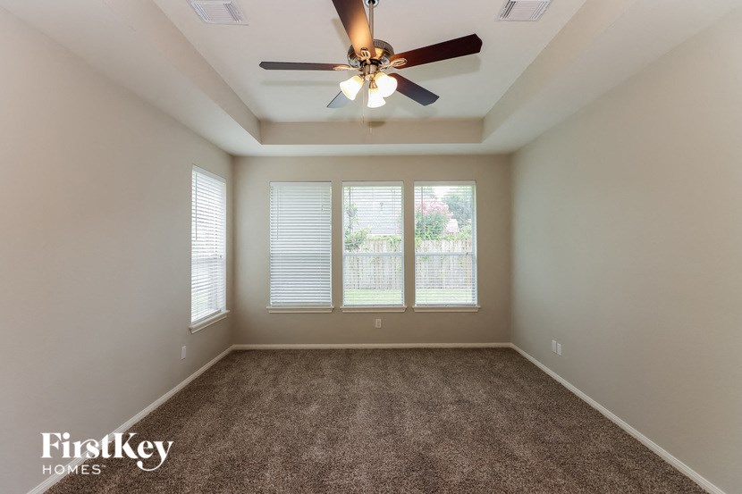 an empty living room with a ceiling fan and three windows