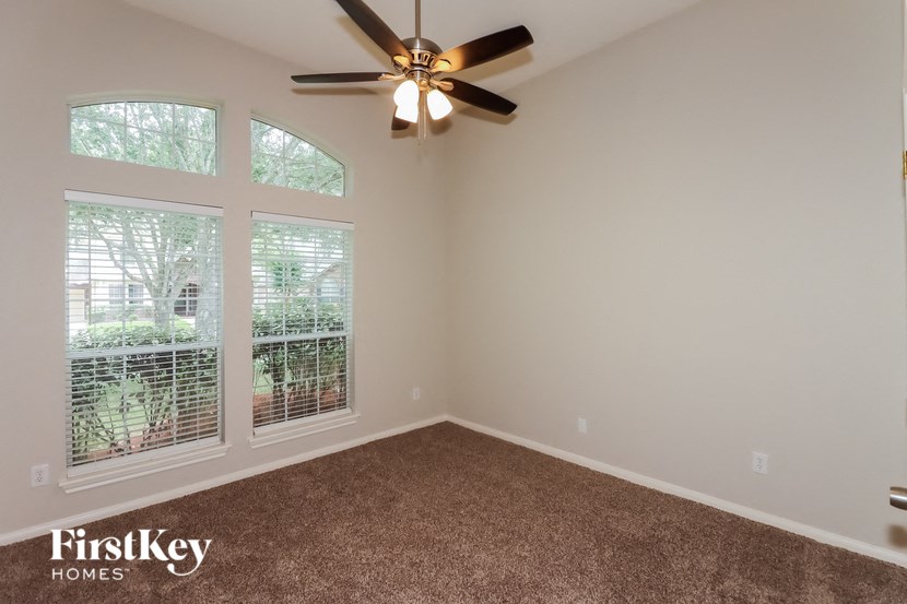 an empty living room with a ceiling fan and three windows
