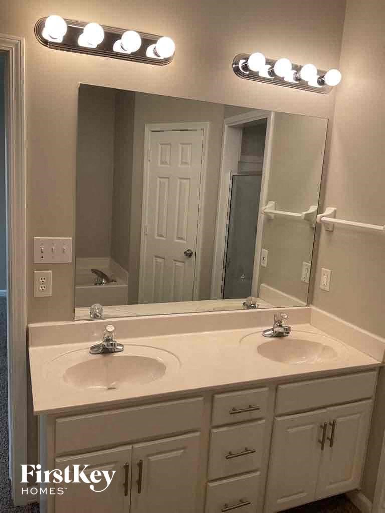 A bathroom with two sinks and a mirror with lights above it.