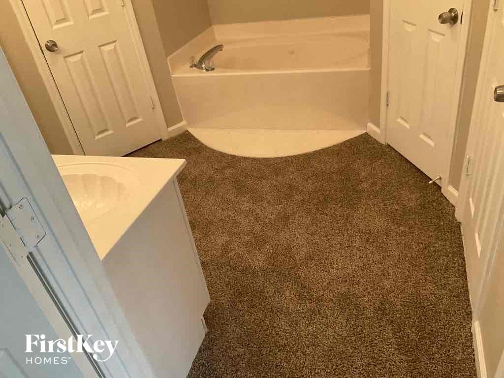 A carpeted bathroom with a bathtub, toilet, and sink.