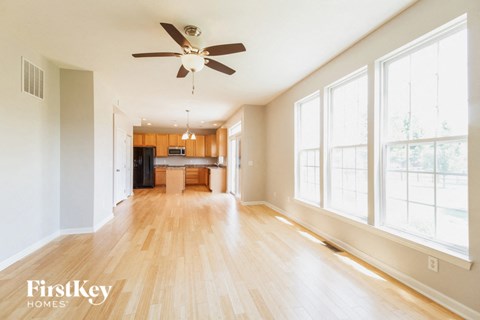 an empty living room with a ceiling fan and a kitchen