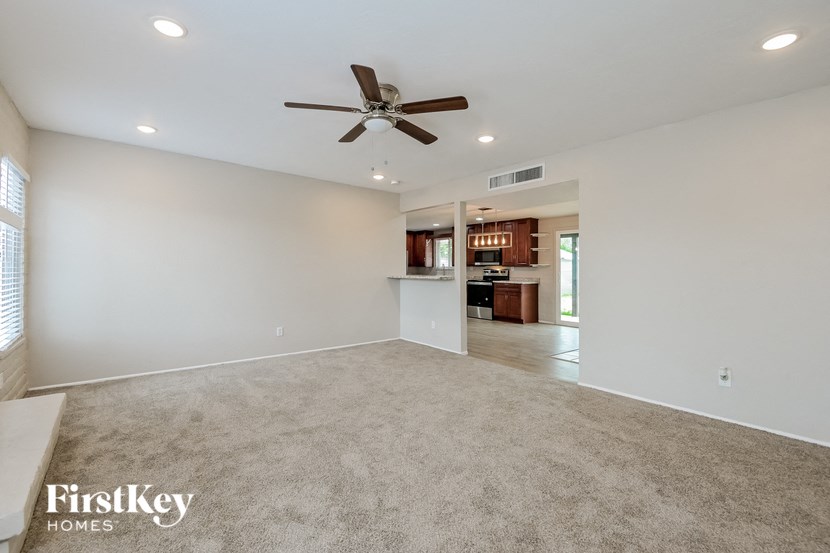 an empty living room with a ceiling fan and a kitchen