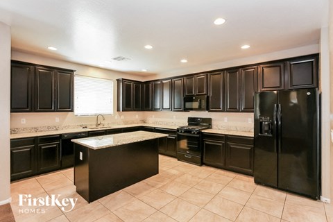 A kitchen with black cabinets and appliances, and a tiled floor.