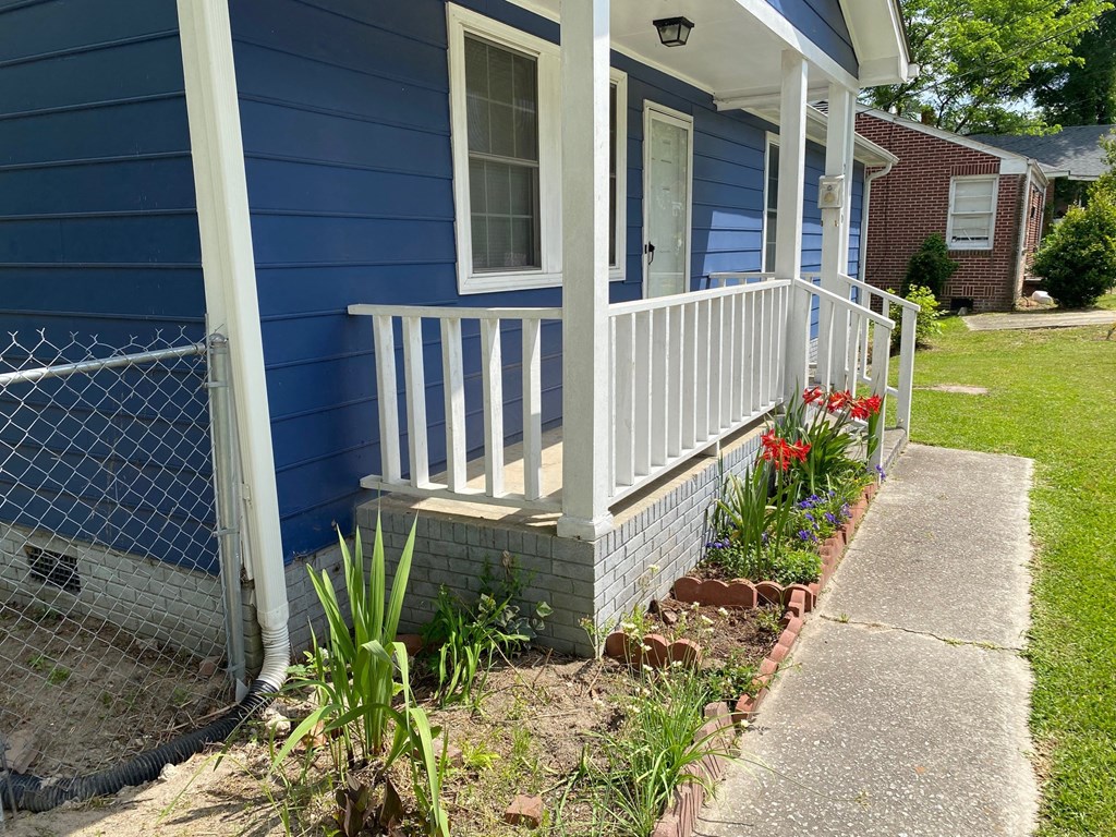 the front porch of a blue house with a white railing and some flowers