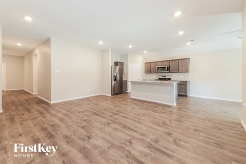 A spacious kitchen with wooden flooring and a refrigerator in the corner.