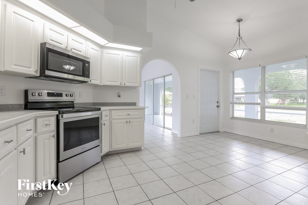 an empty kitchen with white cabinets and white tiled flooring and white appliances