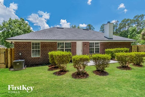 A house with a brick exterior and a chimney is surrounded by bushes.