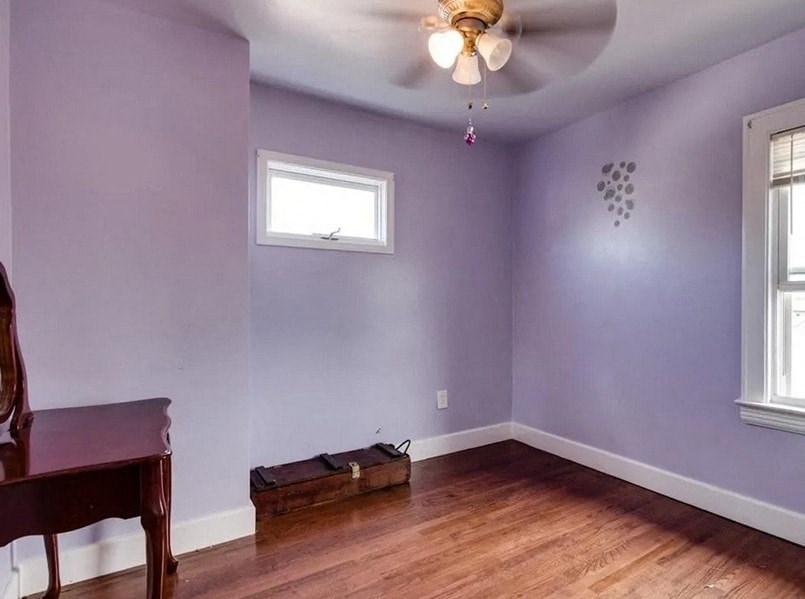 an empty living room with purple walls and a ceiling fan