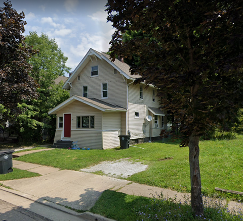A house with a red door is surrounded by greenery.
