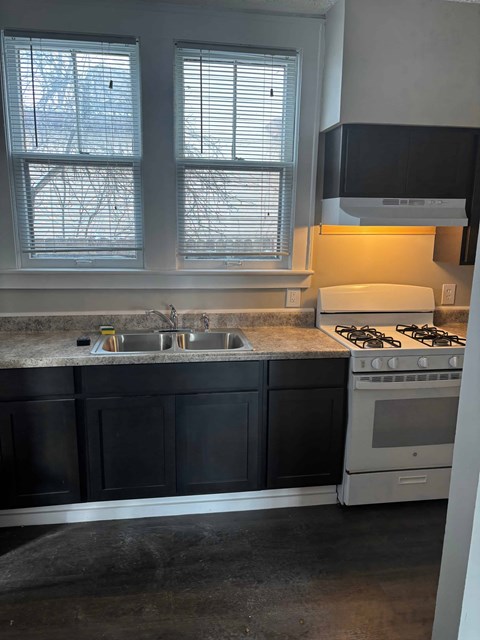 A kitchen with a stove, sink, and cabinets.