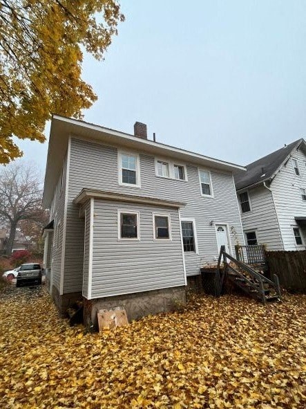 A house with a grey siding and a white door is surrounded by fallen leaves.
