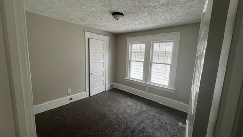 A room with a carpeted floor, a door, and a window with white blinds.