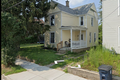A house with a front porch and a trash can in front of it.