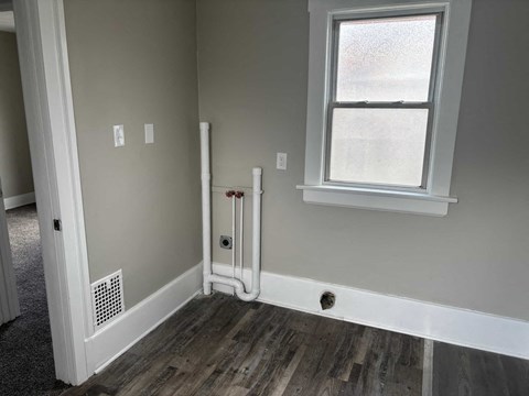 A room with a window, a white door, and a white pipe on the wall.