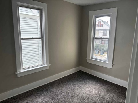 A room with two windows, one of which has a view of a building outside.